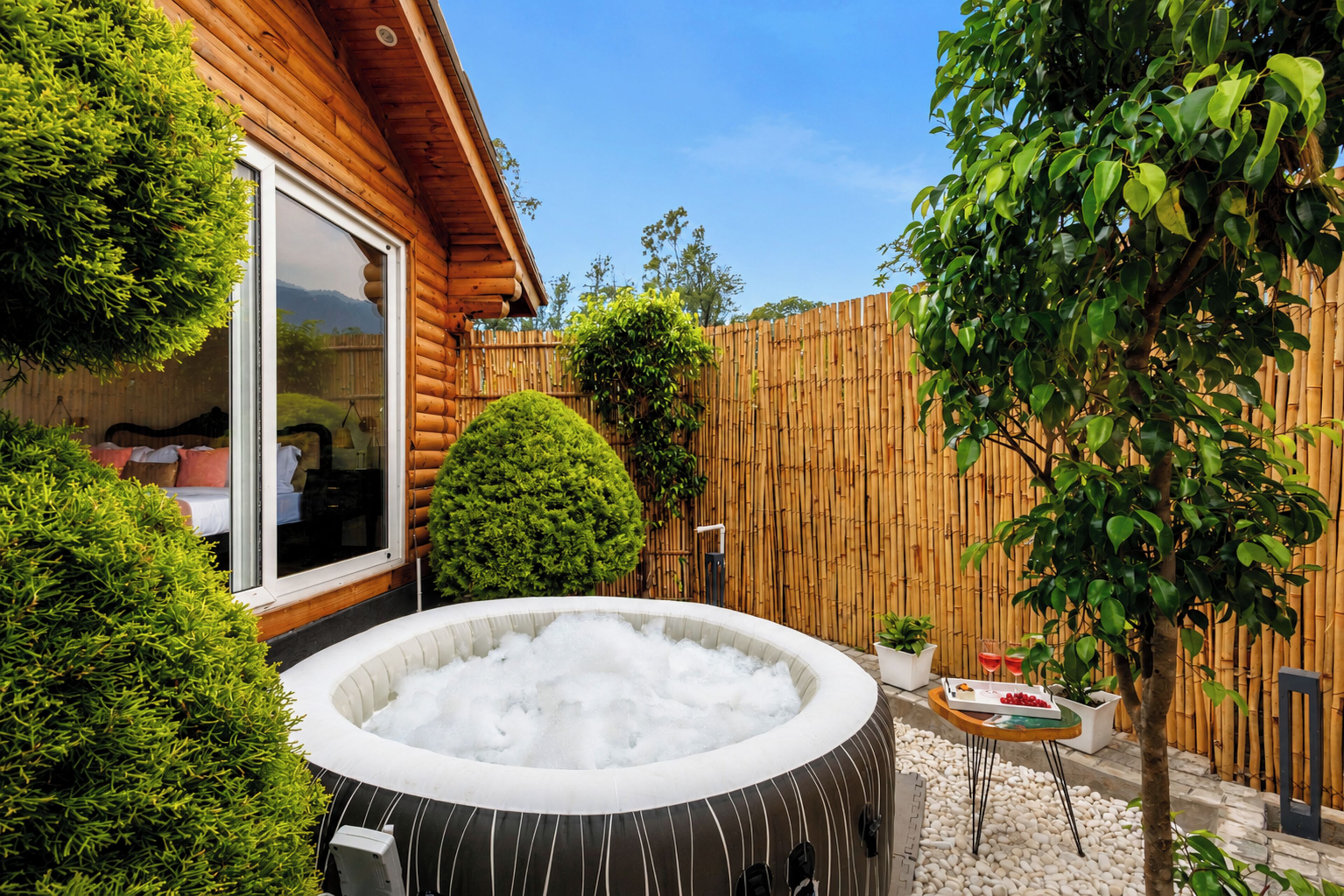 Eine Holzhütte mit Whirlpool, einem eingezäunten Garten und einem kleinen Tisch mit Getränken.
