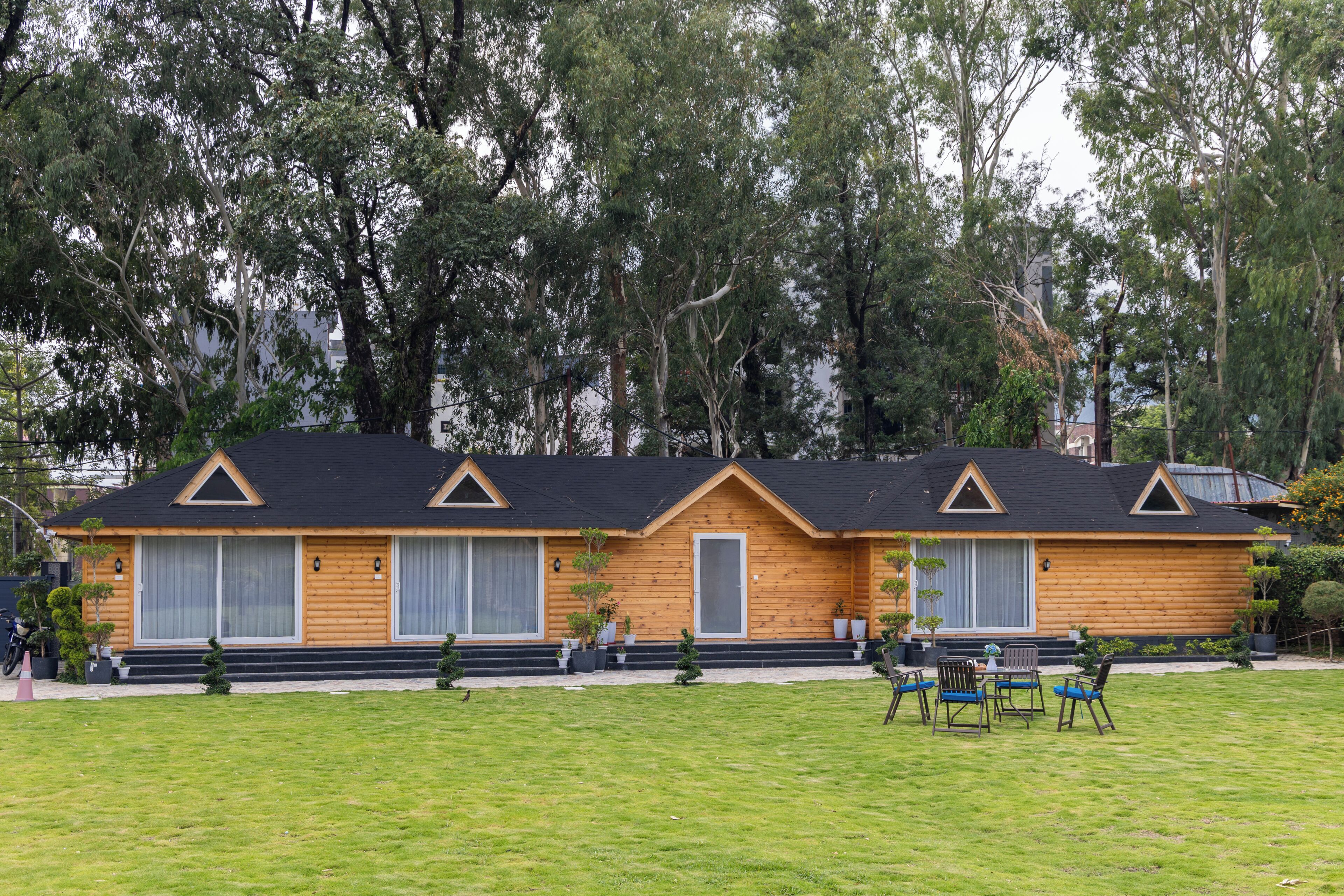 A two-story log cabin with a dark roof, surrounded by a grassy lawn and dense trees.