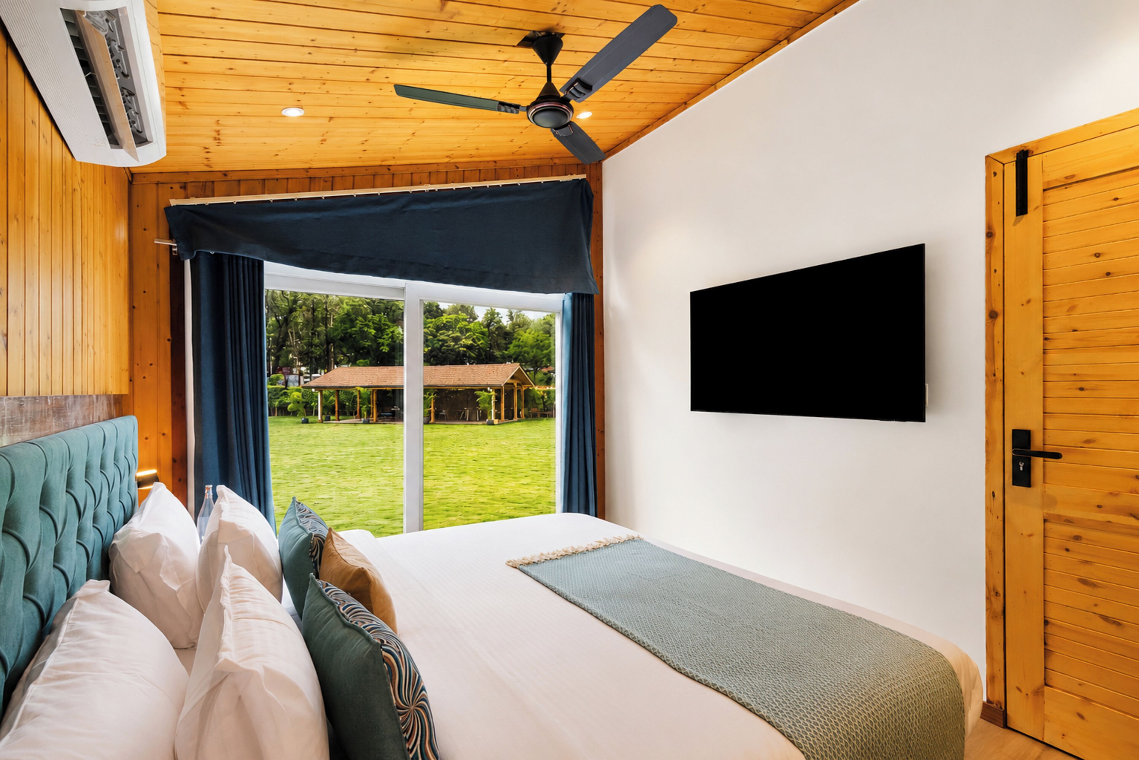 A bedroom with a bed, a ceiling fan, a TV mounted on the wall, and a view of the outdoors.