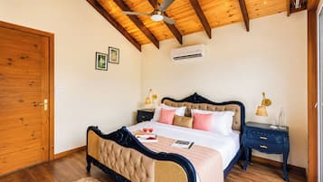 A bedroom with a wooden ceiling, a bed with a dark headboard, two bedside tables with lamps, and an air conditioning unit on the wall.
