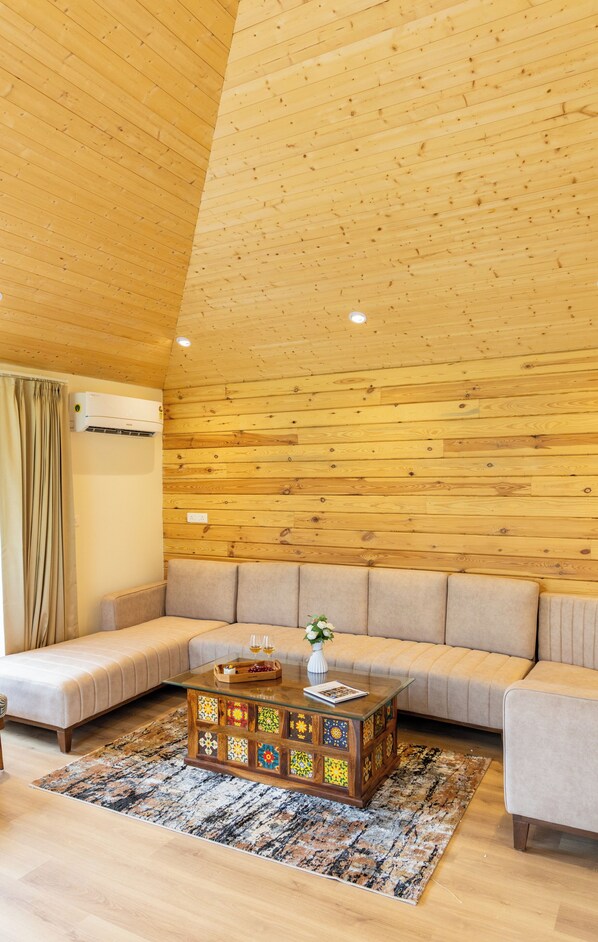 A modern living room with a wooden ceiling, a sofa, a glass coffee table, and a patterned rug.