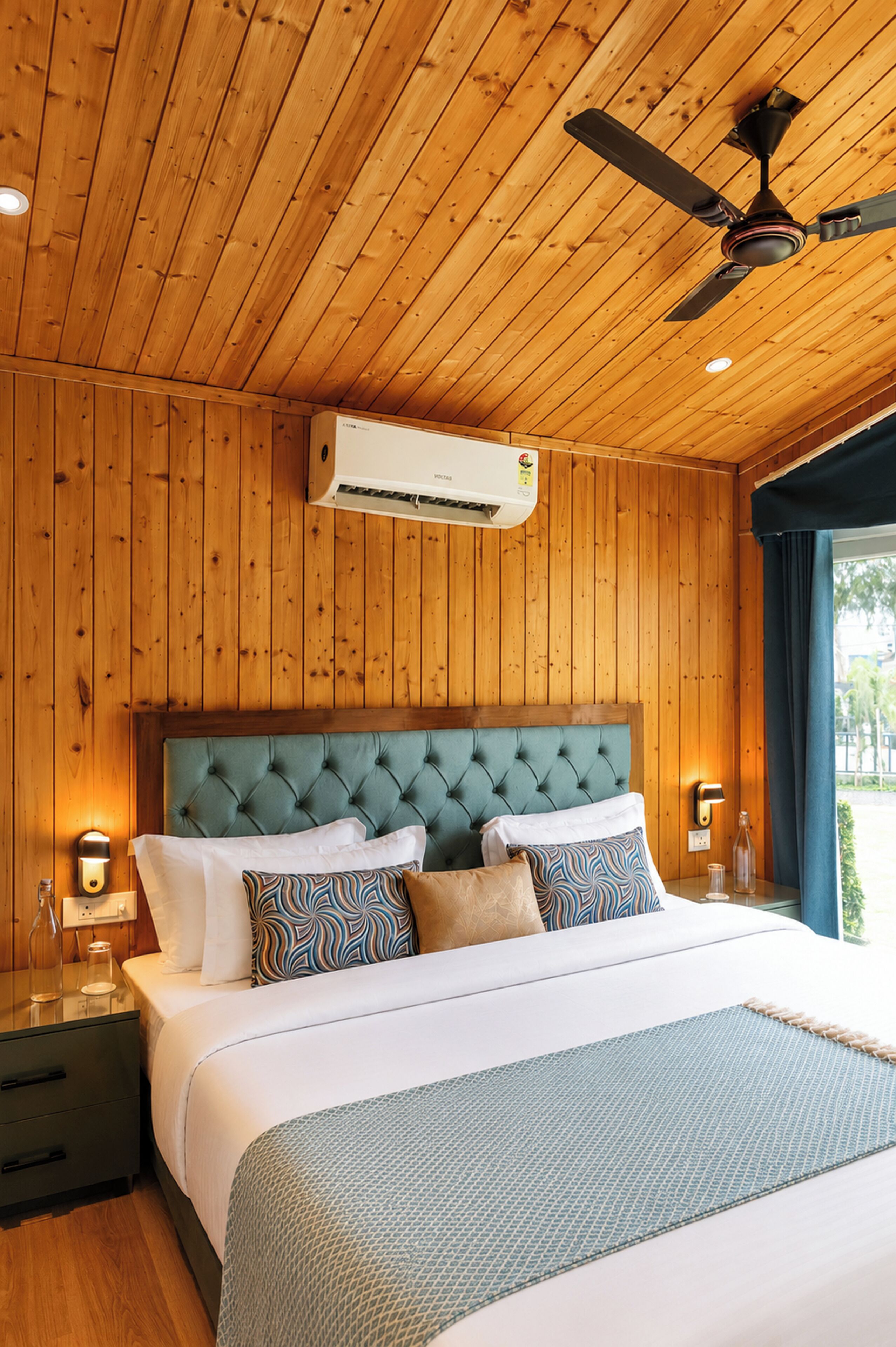A bedroom with a wooden ceiling, a bed with multiple pillows, a nightstand, and a wall-mounted air conditioner.