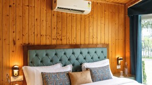 Een slaapkamer met een houten plafond, een bed met veel kussens, een nachtkastje en een aan de muur bevestigde airconditioner.
