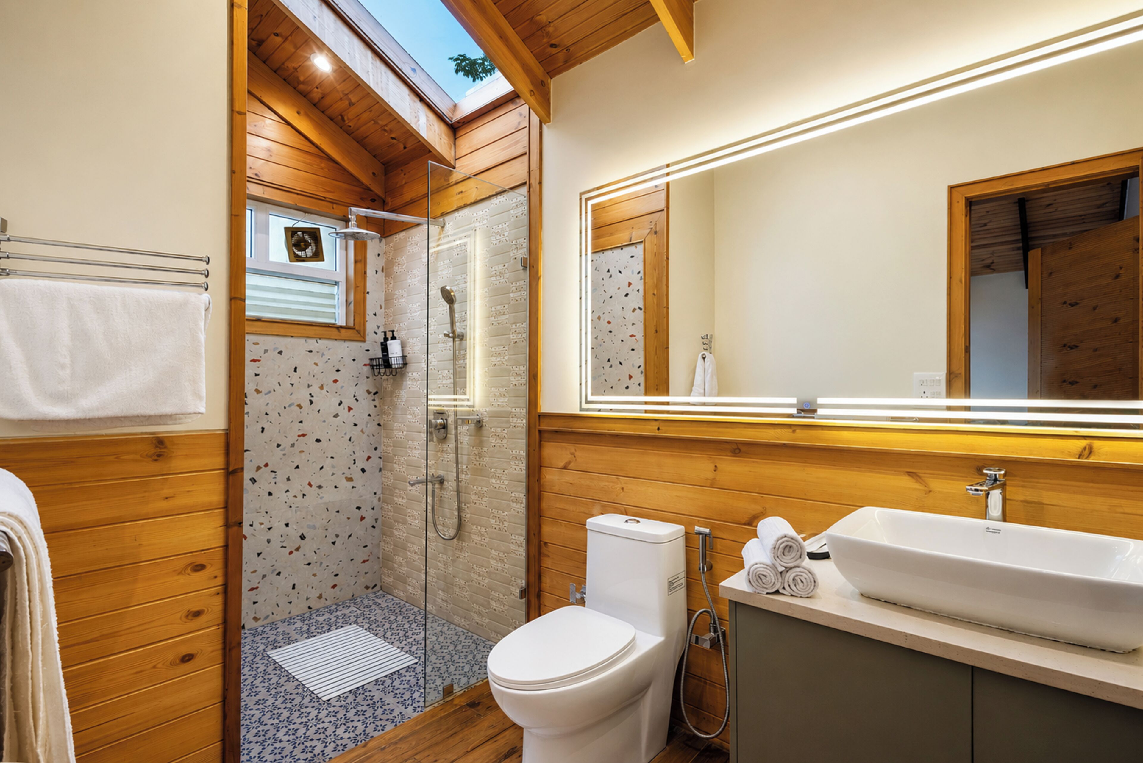 A bathroom with a shower, toilet, and sink, wooden walls, and a skylight.