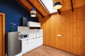 A kitchen with a modern design, featuring a stainless steel refrigerator, a microwave, white cabinets, and a herringbone tile backsplash. - Alaya stays Alora in the hills (Dehradun)