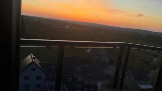 Un balcón con vista a una puesta de sol sobre un barrio residencial.