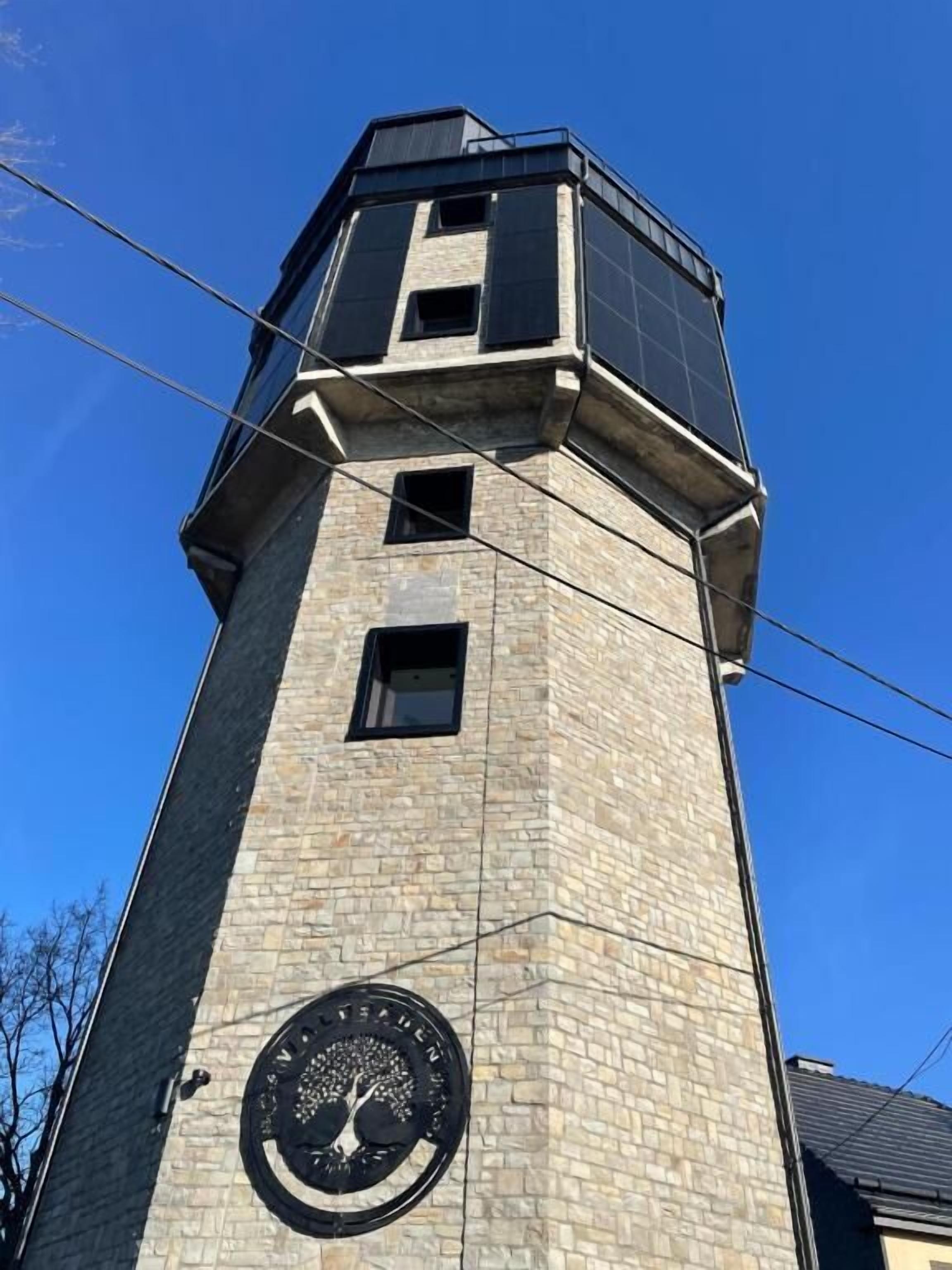 Una alta torre de piedra con un emblema circular en la base, un techo plano y una ventana pequeña.