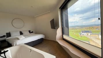 Une chambre moderne dotée d’une grande fenêtre, d’un lit, d’une baignoire intégrée et d’un téléviseur à écran plat.