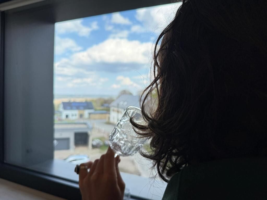 A person holding a clear glass near a window.