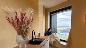 Una cocina moderna con un ventanal grande, un florero con plantas secas y vistas al campo.