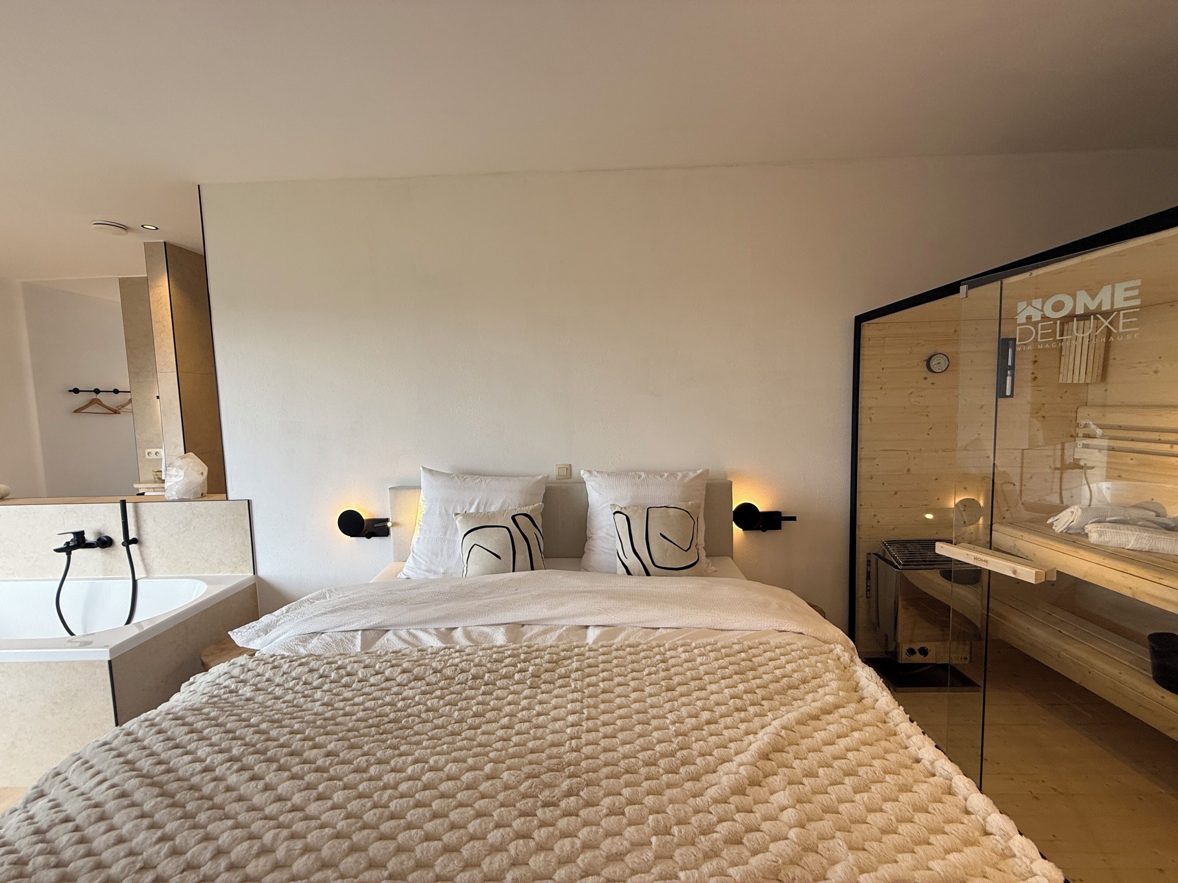 Ein modernes Schlafzimmer mit einem großen Bett, einem Nachttisch, einem Spiegel und einem Glasabtrennung mit Holzinnenraum.
