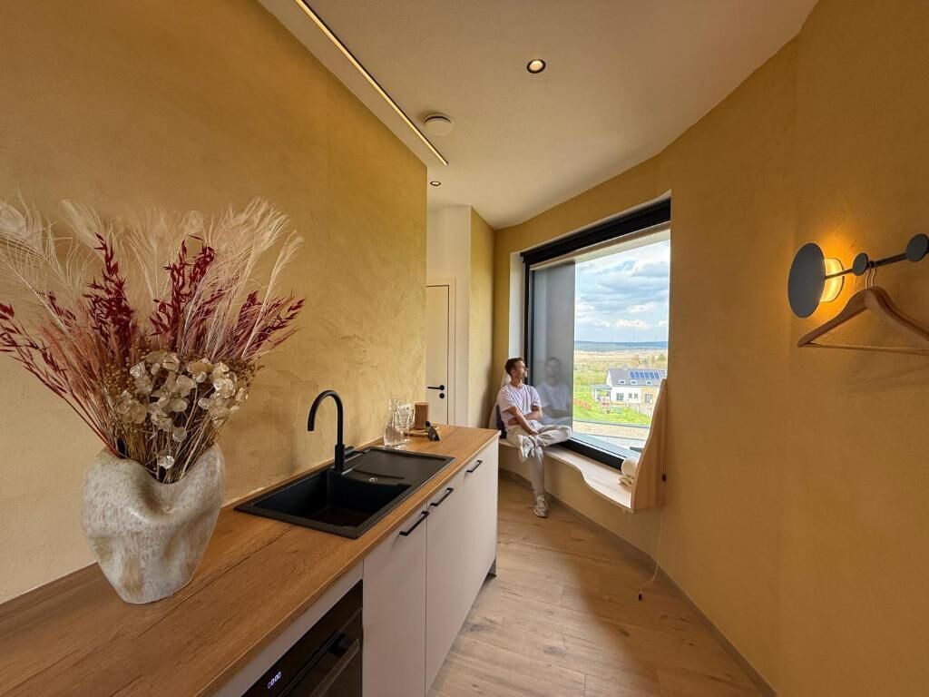 A modern kitchen with a large window, a sink, and a vase of dried plants.