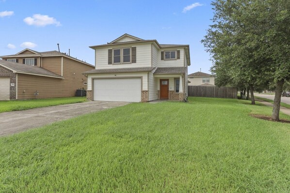 A two-story residential house with a garage, a front lawn, and a wooden fence.