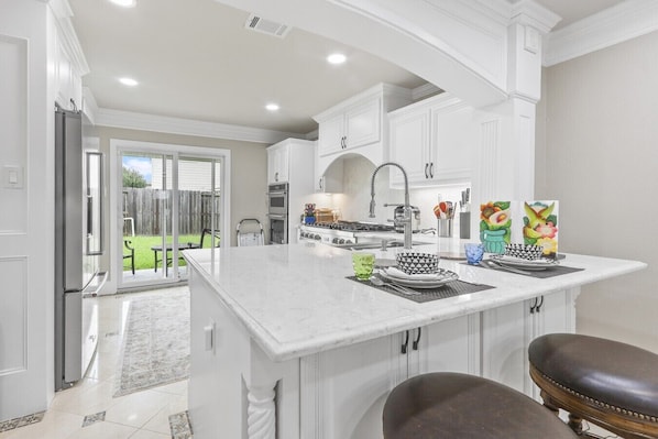 A kitchen with white cabinetry, a central island, and a dining area with a bench. - Sweet Home - Private Room in a Shared Home (Houston)