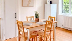 Un coin repas avec une table et des chaises en bois, un luminaire suspendu, un tableau encadré au mur et une fenêtre donnant sur un paysage verdoyant.