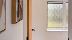 Une salle de bain avec des toilettes blanches, un cadre de porte en bois et une fenêtre à carreaux dépolis.