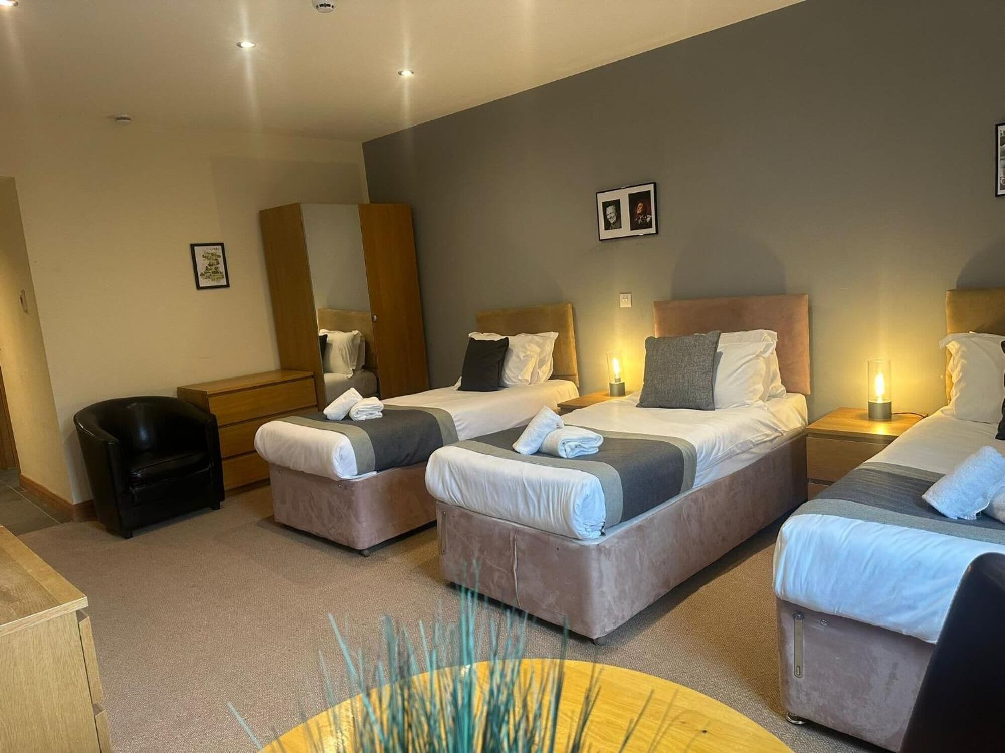 A hotel room with three beds, a desk, a chair, and a small table.