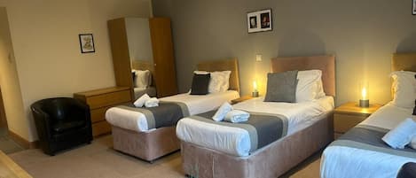 A hotel room with three beds, a desk, a chair, and a small table.