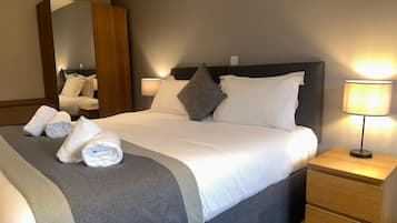 Una habitación de hotel con una cama grande, dos lámparas de noche, una mesita de noche de madera y un espejo.