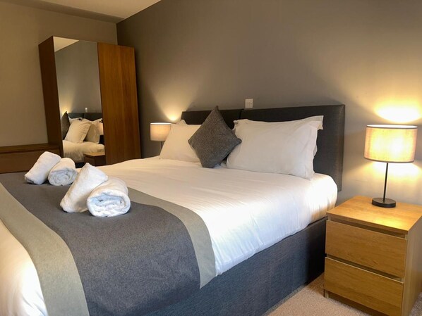 A hotel room with a large bed, two bedside lamps, a wooden nightstand, and a mirror. - Afan Mountain Lodge (Port Talbot)
