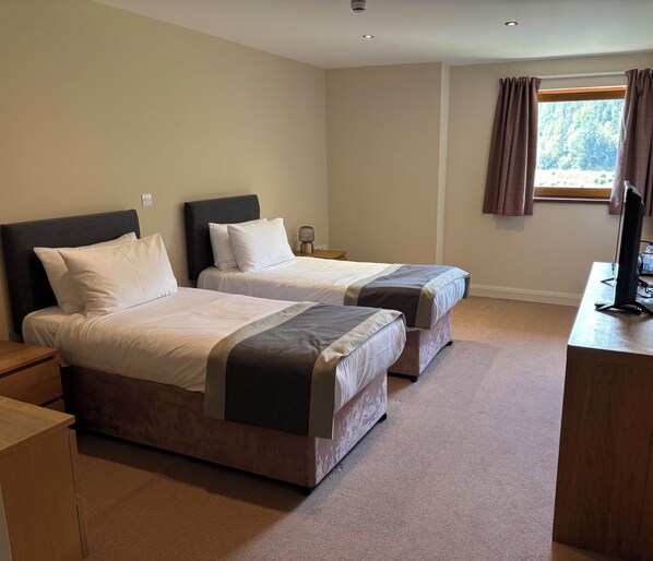 A hotel room with two beds, a desk, a television, and a window with curtains.