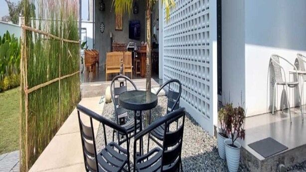 Eine Terrasse im Freien mit Tisch, Stühlen, einer Palme und einem weißen Zaun.