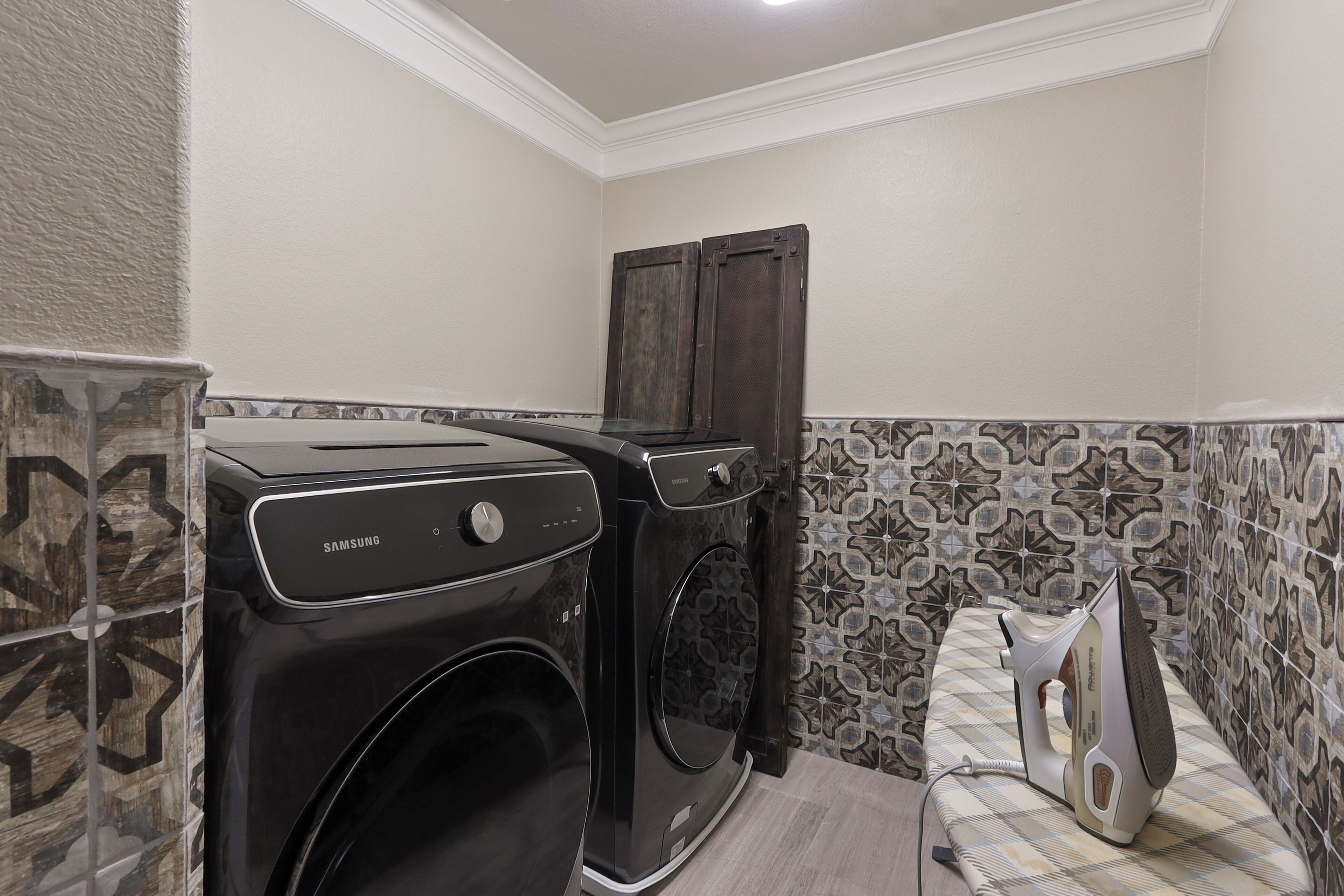 A laundry area with a black washing machine and dryer, a wooden cabinet, and patterned tiles on the walls.