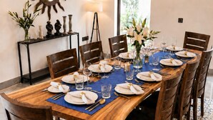 Un'area pranzo con un tavolo in legno apparecchiato per otto persone, circondato da sedie, uno specchio decorativo e un condizionatore d'aria a parete.