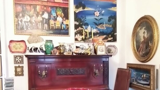 Uma sala de jantar com uma mesa redonda, cadeiras, um vaso vermelho e obras de arte nas paredes.