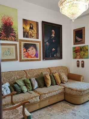 A living room with a large sofa, a chandelier, and various framed artworks on the wall. - Splendida casa Taormina mare (Villagonia)