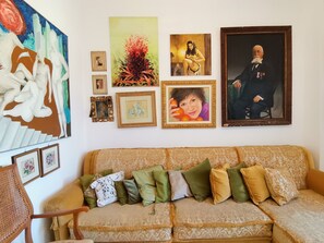 A living room with a sofa, various framed pictures, and a large abstract painting. - Splendida casa Taormina mare (Villagonia)