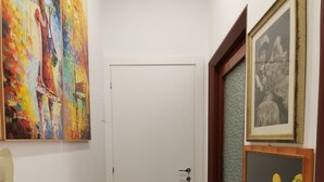 Um corredor com porta branca, piso de azulejos e obras de arte nas paredes.