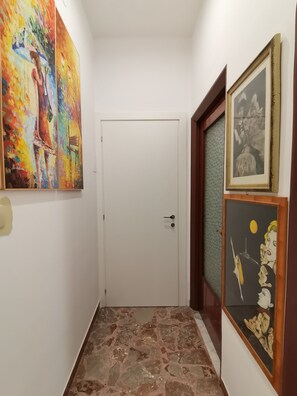 A hallway with a white door, a tiled floor, and artwork on the walls. - Splendida casa Taormina mare (Villagonia)