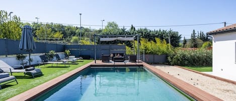 A rectangular swimming pool with a wooden deck, surrounded by a grassy area with lounge chairs.