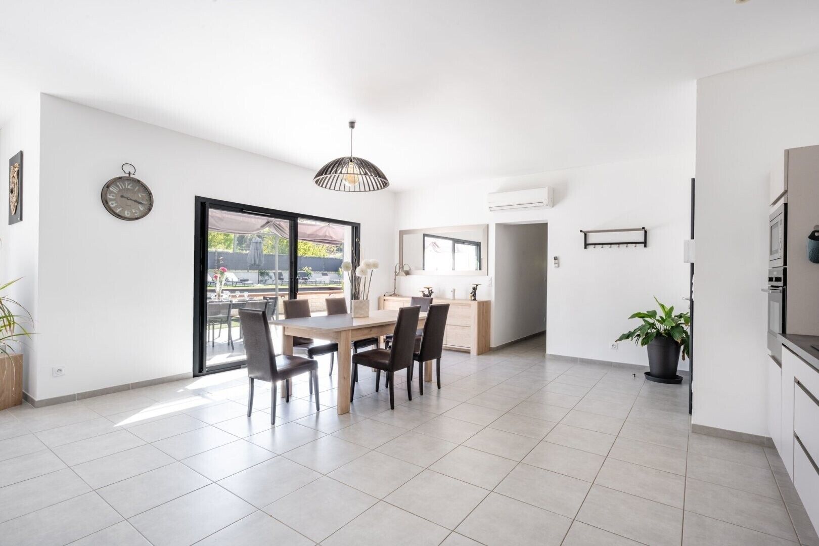 A modern kitchen with a dining area, a clock on the wall, and a large window.