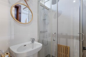 Casa de banho com lavatório branco, espelho e cabine de duche com parede de vidro.