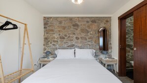 Ein Schlafzimmer mit Steinwand, einem Bett mit weißer Bettwäsche, zwei Nachttischen mit Lampen, einem Holzschrank und einem Kleiderständer aus Holz.