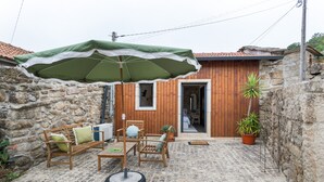 Ein Sitzbereich im Freien mit Stehwänden, einem Holztisch, Stühlen, einem Reifen-Sitzhocker und einem grünen Sonnenschirm.