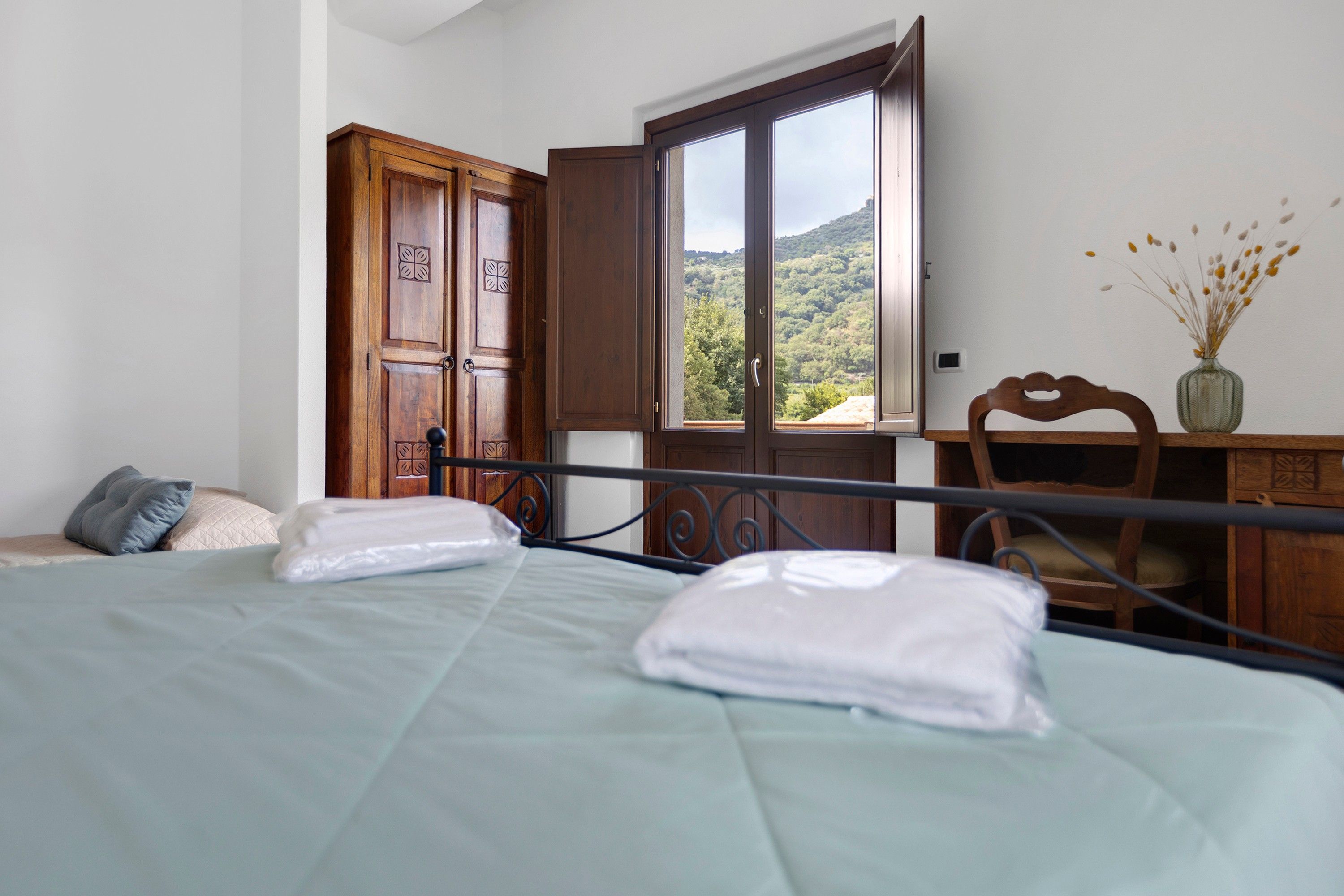 Une chambre à coucher comprenant un lit, une armoire en bois, un bureau avec une chaise et une fenêtre donnant sur une colline.