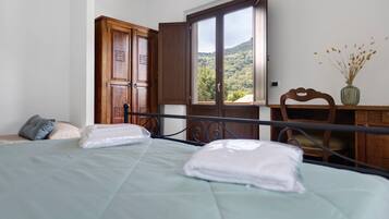 Une chambre à coucher comprenant un lit, une armoire en bois, un bureau avec une chaise et une fenêtre donnant sur une colline.