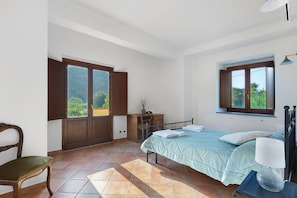 A bedroom with a bed, a chair, a desk, and a window.
