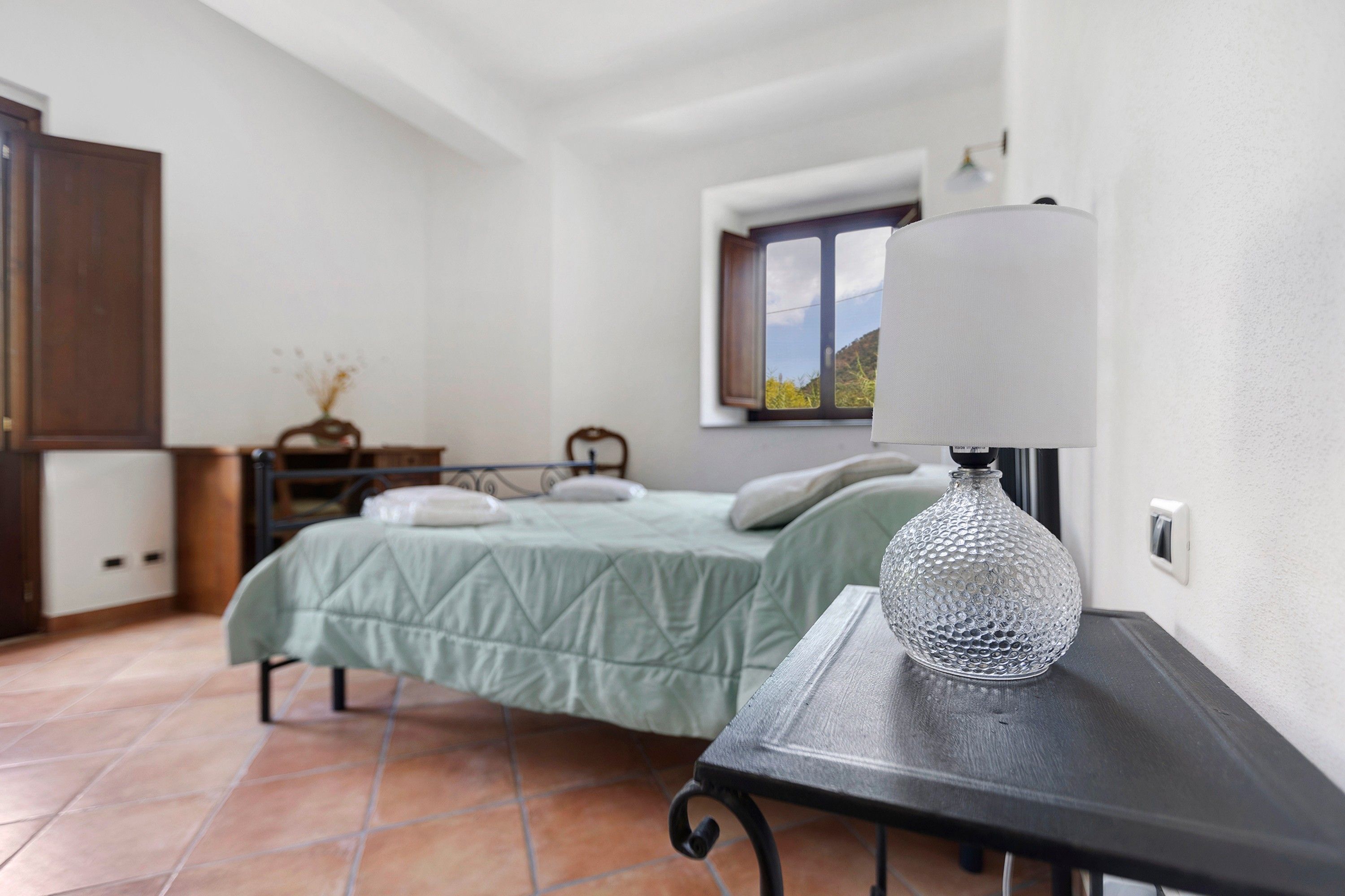 Quarto com cama, mesa de cabeceira e janela com vista.