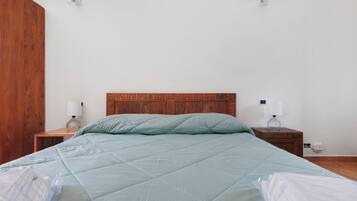 Une chambre à coucher avec une tête de lit en bois, un lit recouvert d’une courtepointe, deux tables de chevet avec des lampes et une prise de courant murale.