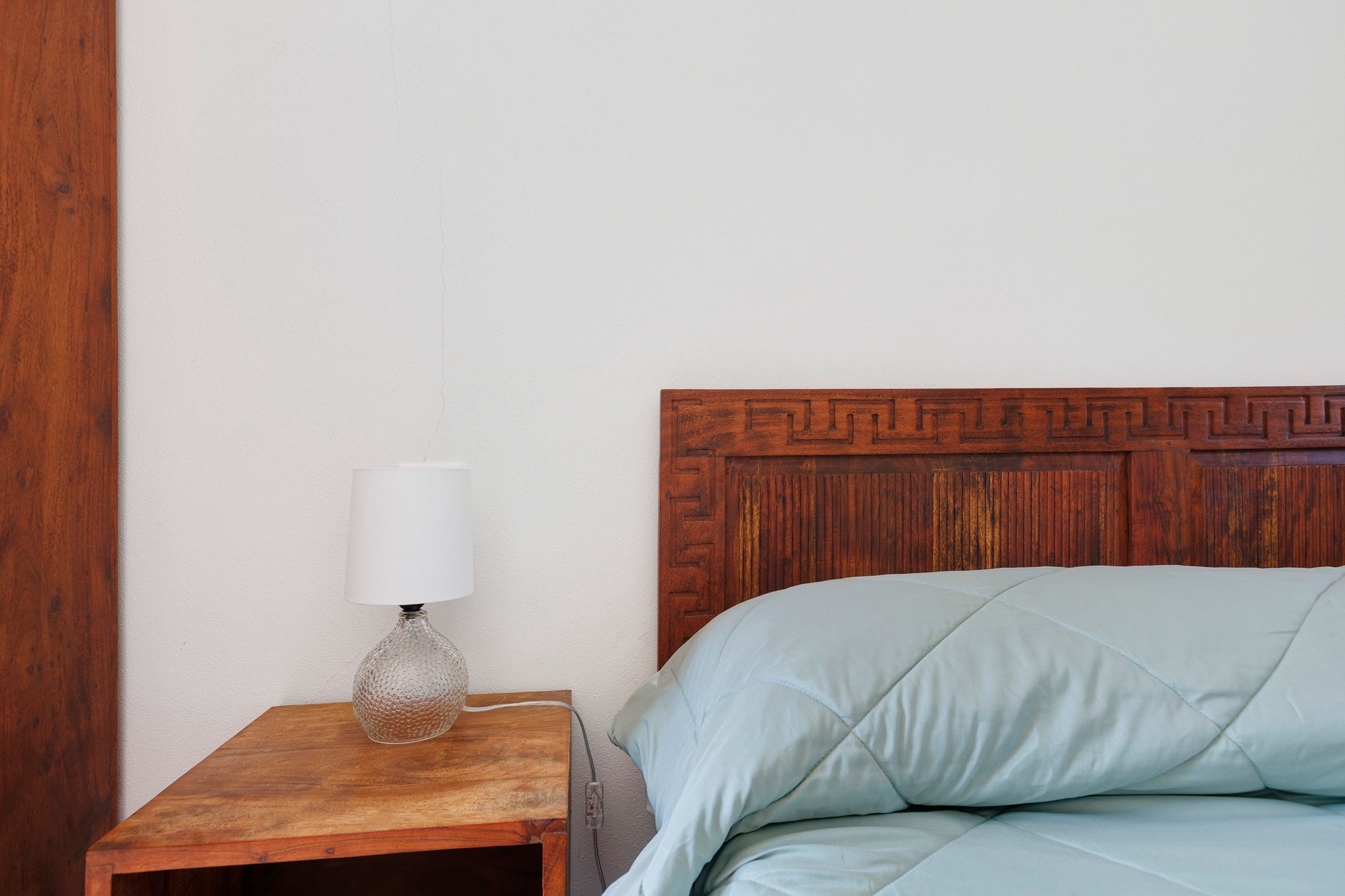 Ein Nachttisch aus Holz mit einer Lampe und ein Bett mit gesteppter Kopfteil.