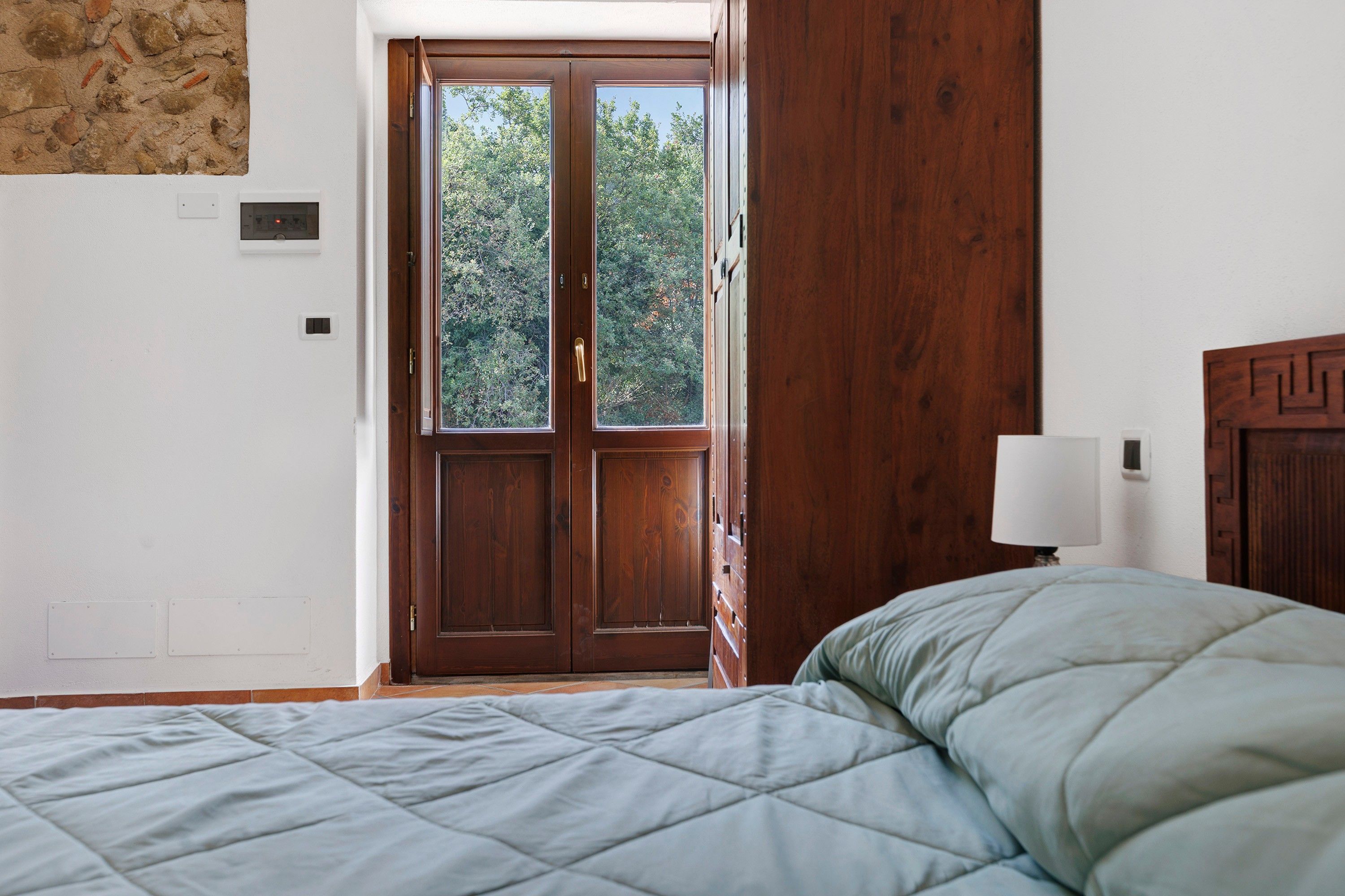 Une chambre à coucher avec un lit, une porte en bois et une vue sur les arbres à l’extérieur.