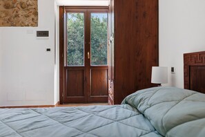 Une chambre à coucher avec un lit, une porte en bois et une vue sur les arbres à l’extérieur.
