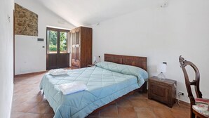 Ein Schlafzimmer mit einem Bett, einem Nachttisch aus Holz, einem Sessel und einer Tür, die nach draußen führt.
