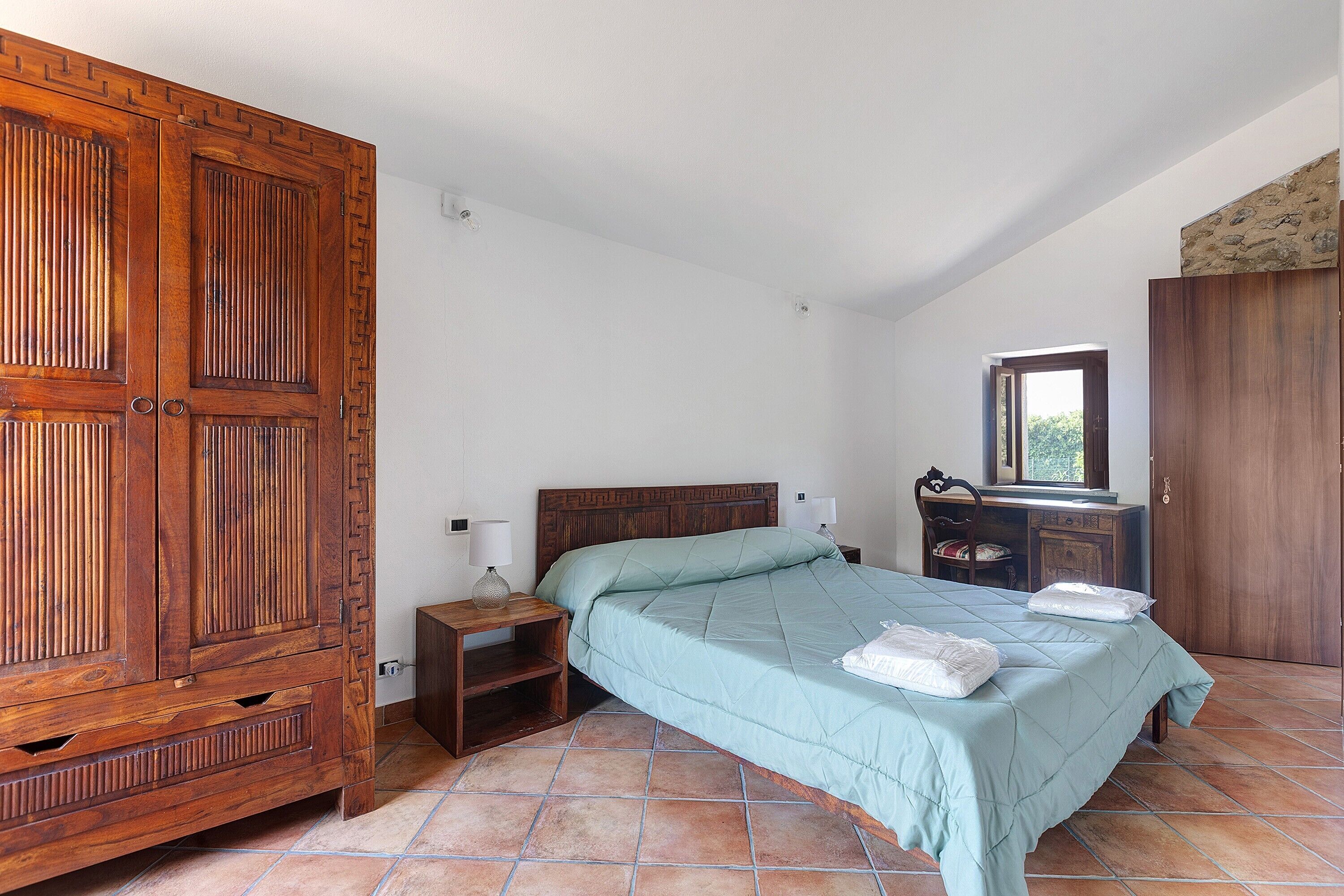Quarto com um arm ário de madeira grande, uma cama com colcha, uma mesa de cabeceira e um penteou com espelho.