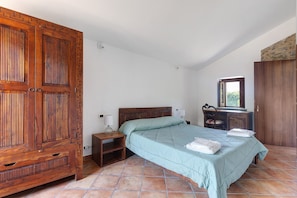 Un dormitorio con un armario de madera grande, una cama con colcha, una mesita de noche y un aparador con espejo.