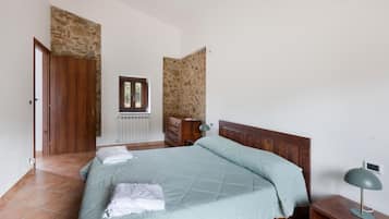 A bedroom with a bed, a wooden wardrobe, a radiator, a window, and a lamp.